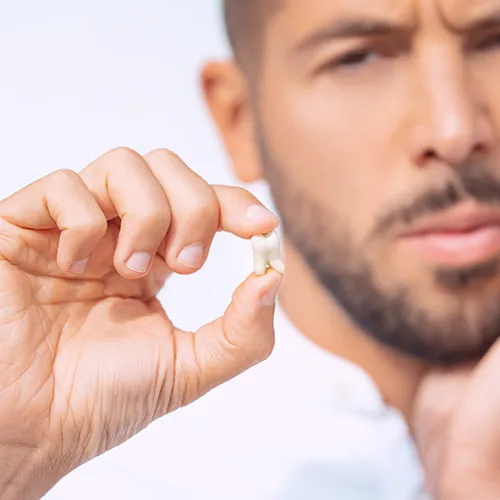 man holding his cheek in one hand and extracted tooth in the other hand