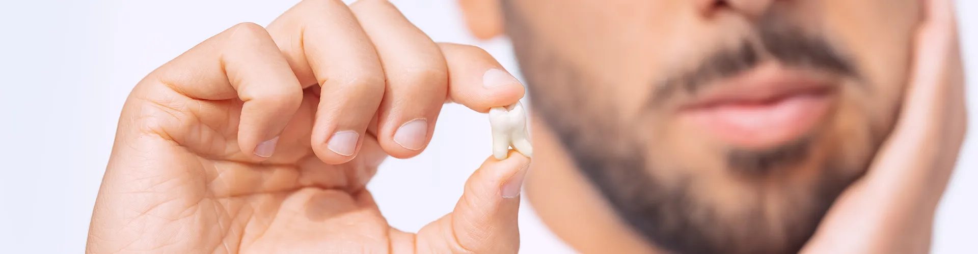 man holding his cheek in one hand and extracted tooth in the other hand