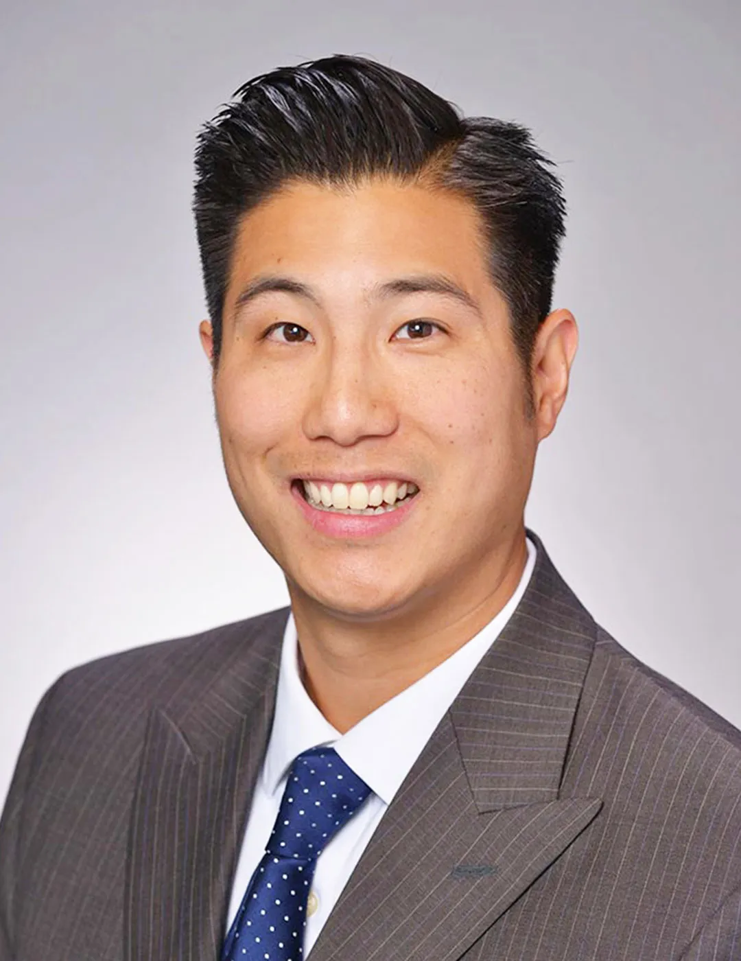 A professional headshot of Dr. Jeremy Owyoung, an Asian male dentist with short black hair, dressed in a dark gray suit and blue polka-dot tie. 