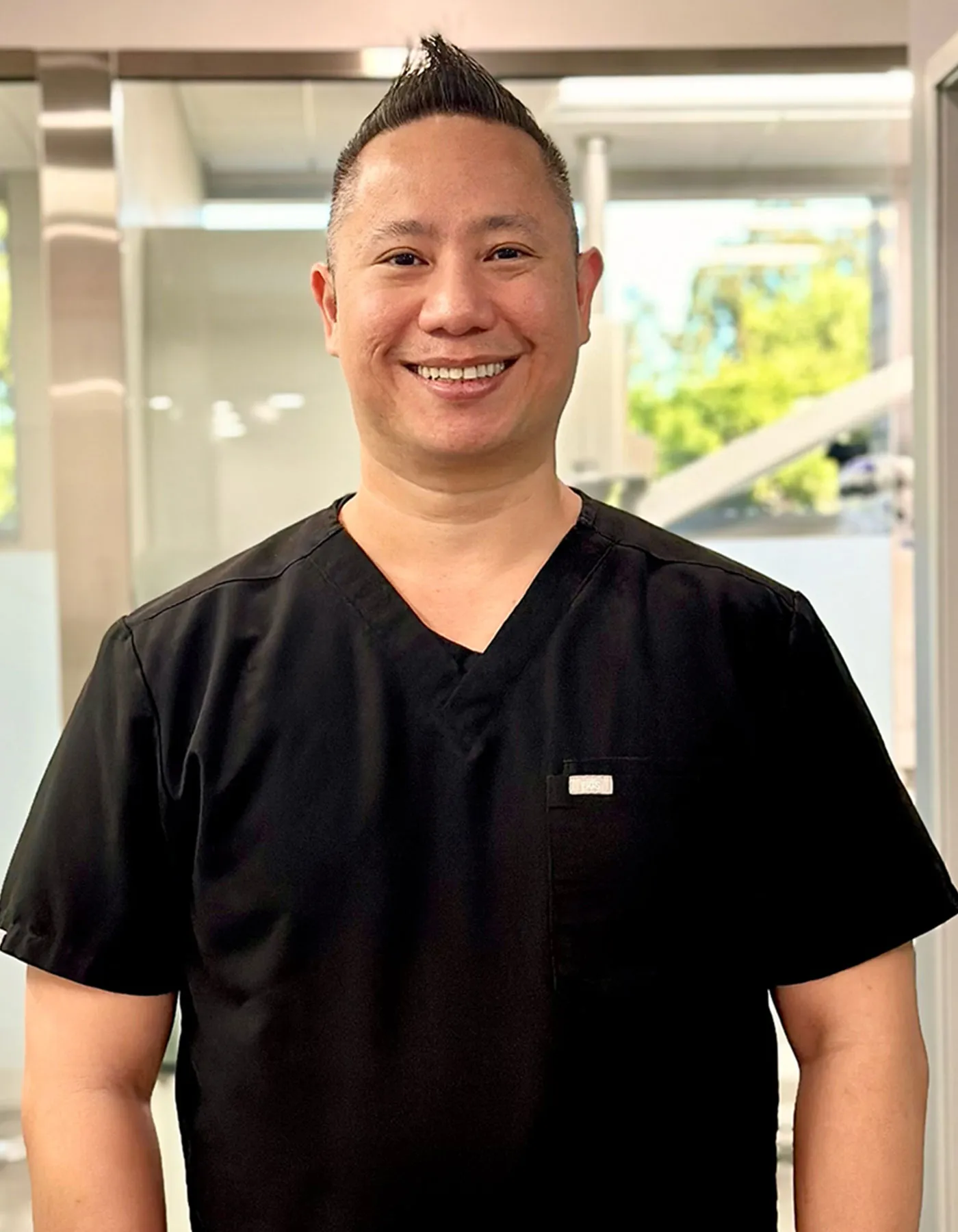 Portrait of Dr. Jimmy Pham wearing black scrubs, standing in a dental office.