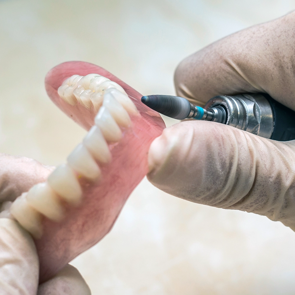 Photo of a dental technician adjusting a set of upper and lower denture plates, showcasing the tools and precision required in denture fabrication.