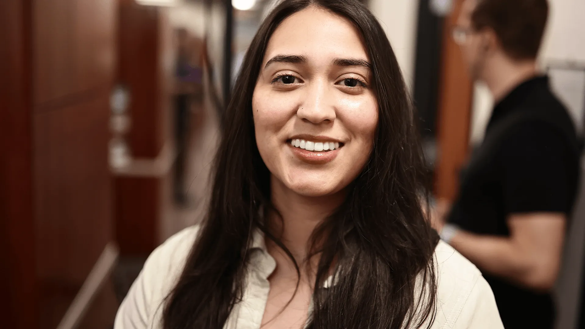 A smiling woman with long dark hair, standing in a dental clinic, representing a satisfied patient after receiving dental veneers.