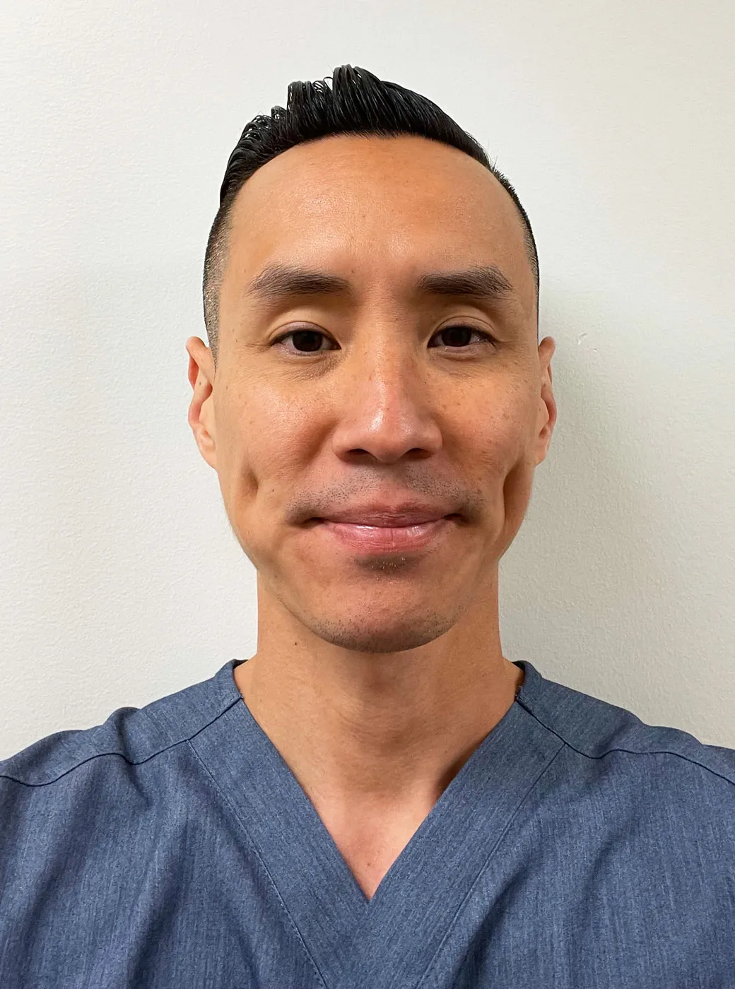 A portrait of Dr. Richard Lee, a male dentist with short black hair, wearing blue dental scrubs.