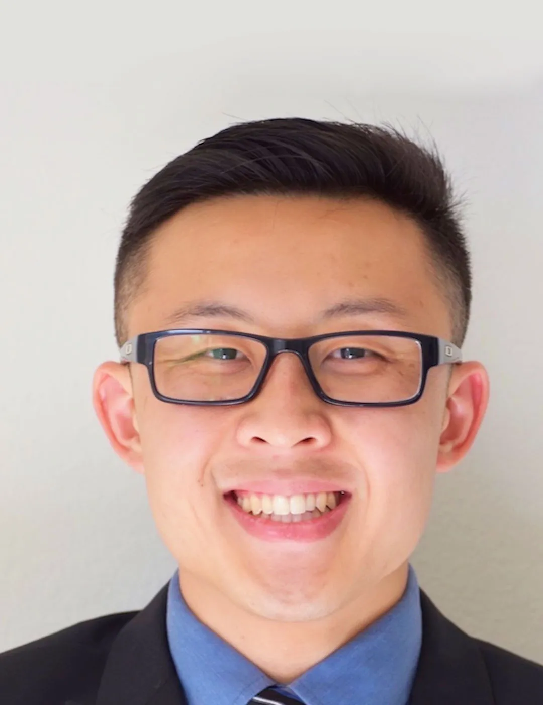 A headshot of Dr. Tran in glasses and a navy blue suit, smiling warmly, which conveys his friendly and professional demeanor.